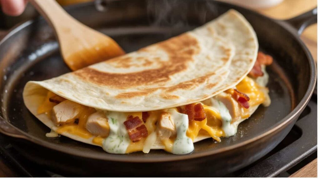 “Assembling chicken bacon ranch quesadilla with cheese and filling on a skillet.”“Chicken bacon ranch quesadilla cooking in a skillet, showing crispy golden tortilla and melted cheese.”